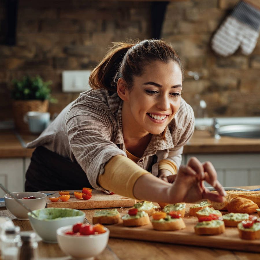 Mujer joven en la cocina preparando sándwiches de canapé montaditos