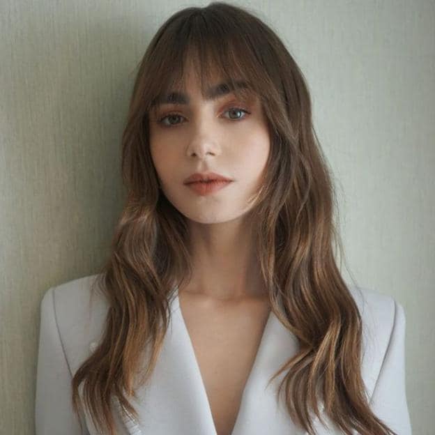 Lily Collins con cabello largo ondulado y flequillo contundente