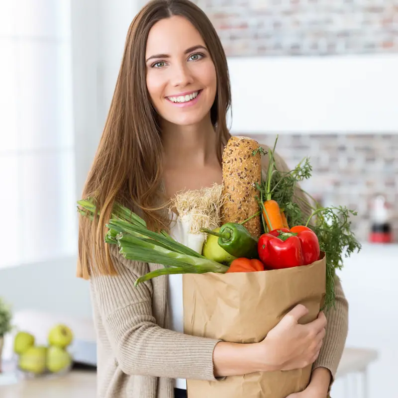 Mujer con una bolsa llena de verduras.