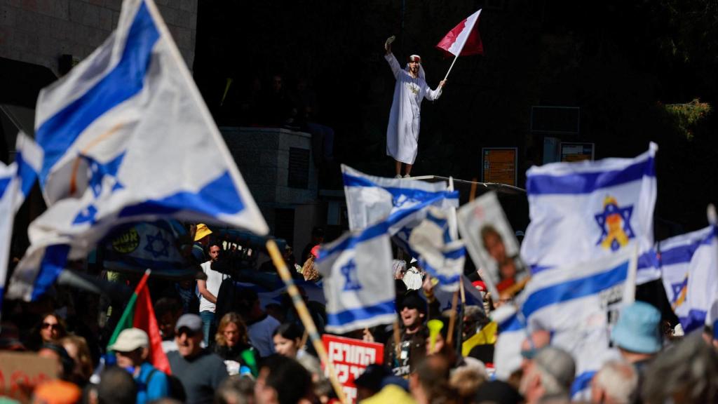 La gente saluda las banderas en una manifestación contra el primer ministro israelí, Benjamin Netanyahu, y su gobierno, donde los manifestantes exigen la liberación de todos los rehenes de Gaza, cerca de la residencia de Netanyahu en Jerusalén.