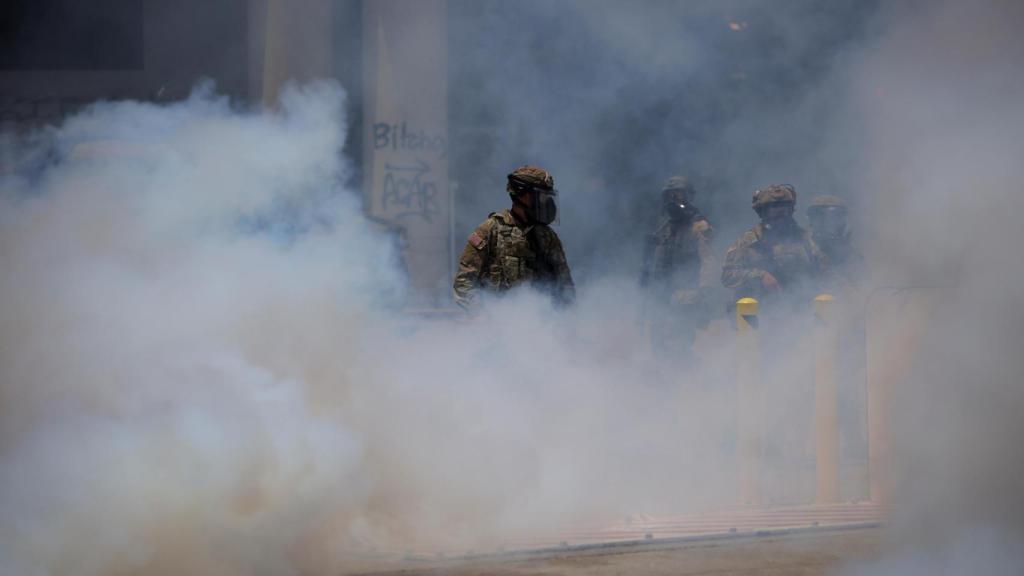 El humo aumenta mientras los miembros de la Guardia Nacional de California se reúnen durante una protesta contra las redadas de inmigración federal en el centro de Los Ángeles,