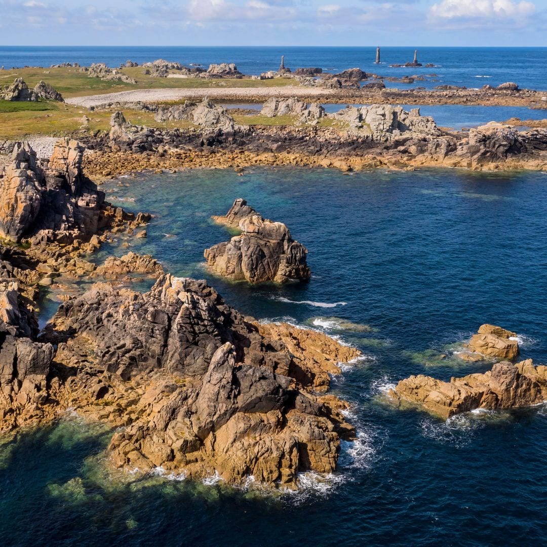 Roches esculpidos por tormentas al pie del Faro de Créac'h, con el faro nivvídico en la punta de Pern al fondo, Bearing Island, Brittany, Francia, Francia