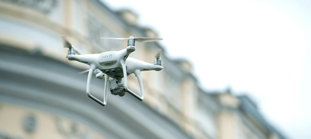 Un dron blanco sobrevuela una zona urbana densamente poblada, ejemplo de operación que requiere un permiso especial de AESA