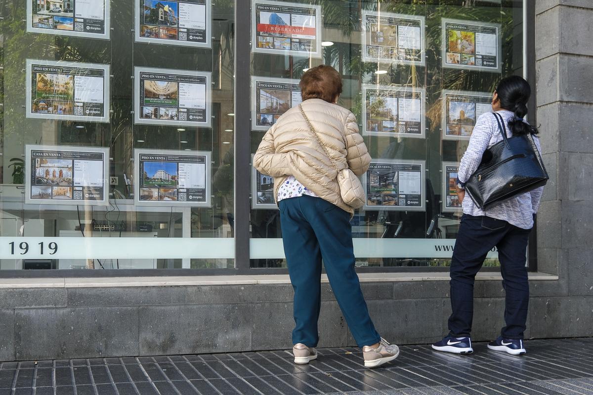 Varias personas miran casas en venta en el escaparate de una agencia inmobiliaria.