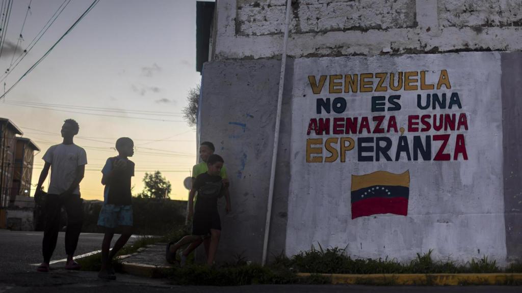 Jóvenes caminan junto a un mural en Caracas.