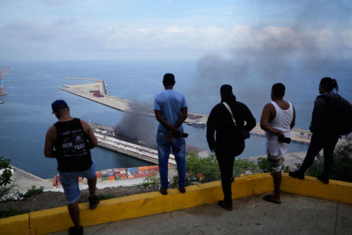 Hombres observan el humo que se eleva desde un muelle después de que se escucharon explosiones en el puerto de La Guaira, Venezuela, el sábado 3 de enero de 2026. (Foto AP/Matías Delacroix). USO EDITORIAL SÓLO/SÓLO ITALIA Y ESPAÑA