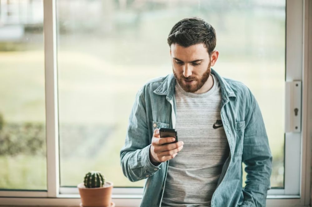 Hombre apoyado en la ventana mediante teléfono móvil