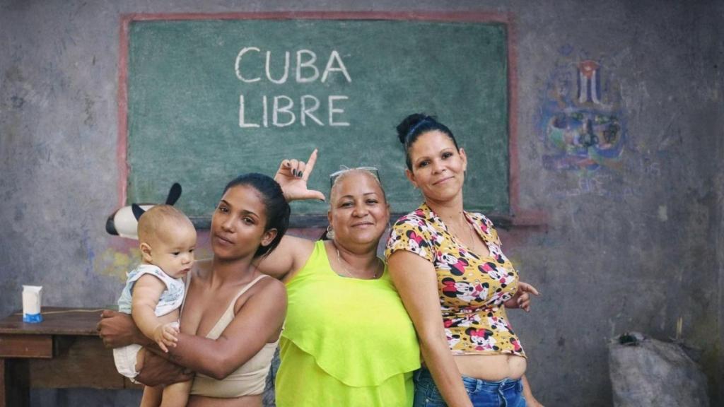 Yadira hace la señal de libertad rodeada de sus hijas en su casa de Las Tunas (Cuba).