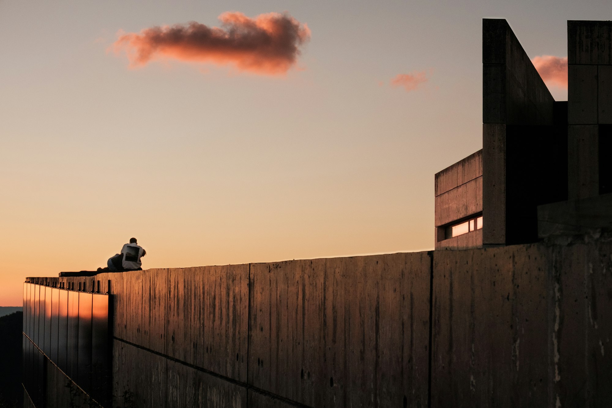 Persona sentada sobre un muro de hormigón al atardecer