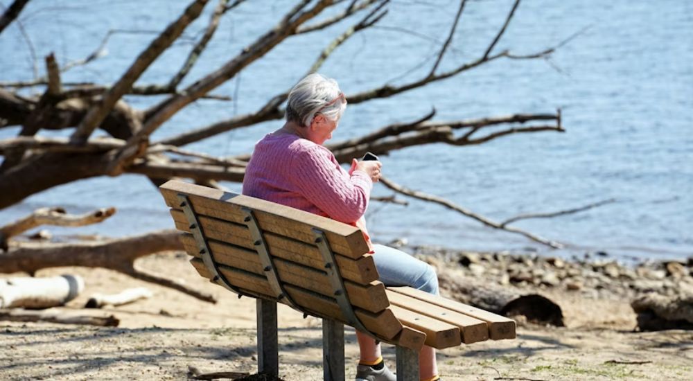 Mujer mayor usando un teléfono inteligente mientras está sentada en un banco