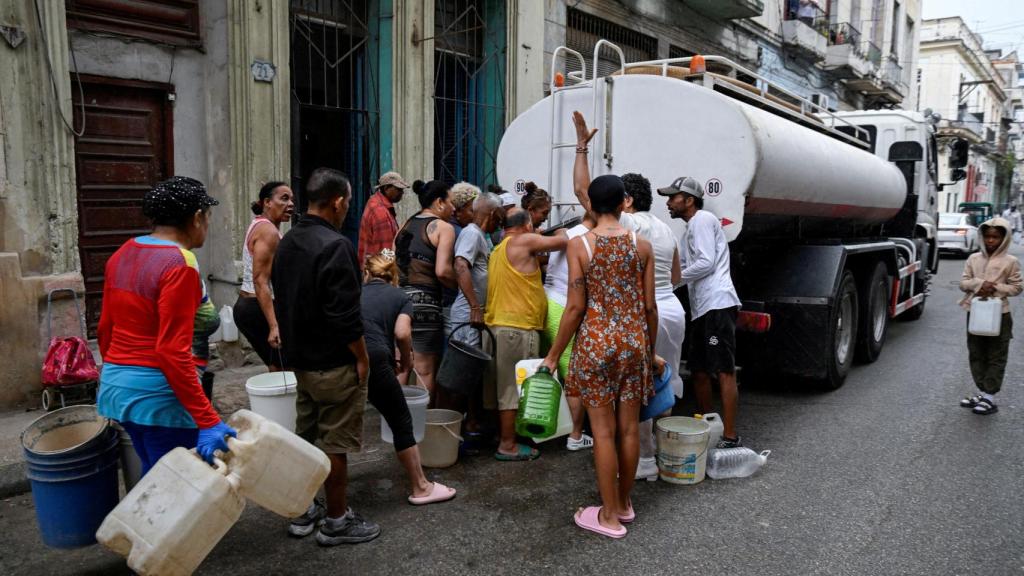 Varias personas se reúnen alrededor de un camión cisterna para llenar cubos y otros contenedores, ya que la grave escasez de combustible ha interrumpido el bombeo y la distribución de agua, en La Habana, Cuba, el 19 de marzo de 2026.