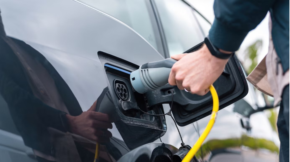 Hombre enchufando el cargador al coche eléctrico en la estación de carga. Foto: Freepik. KIA.
