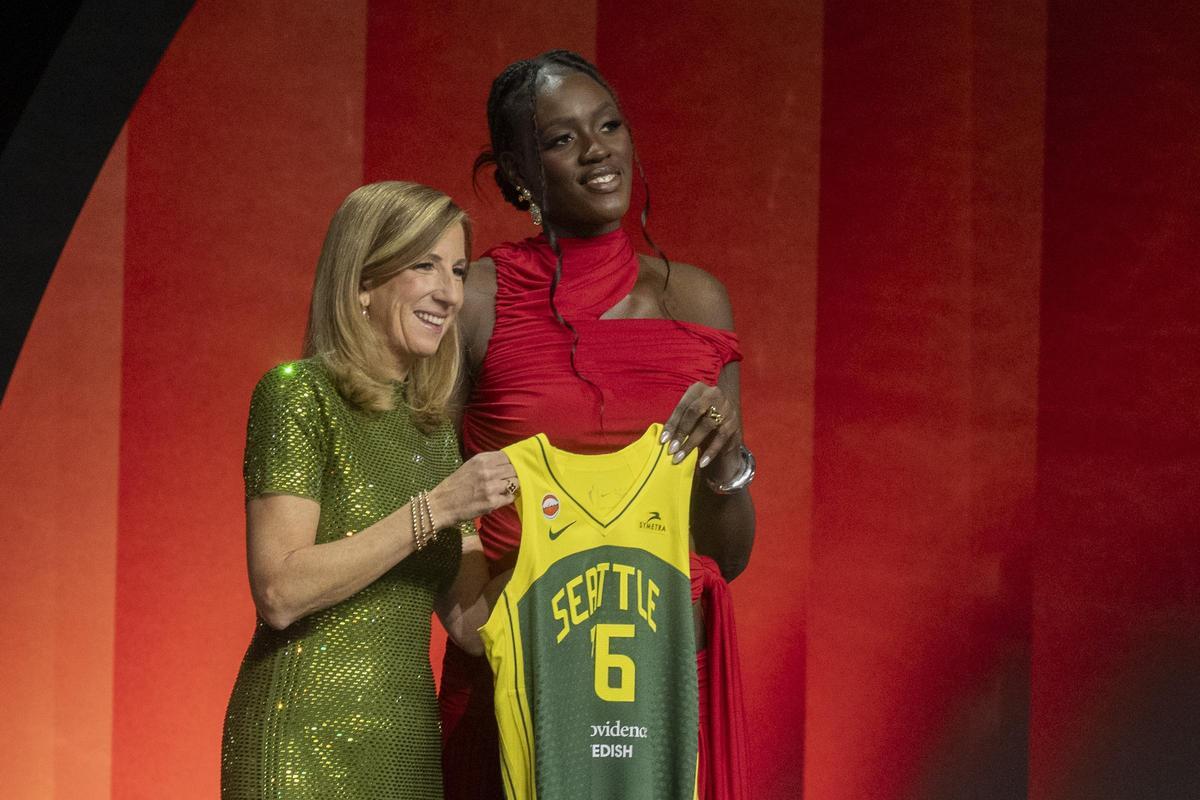 La comisionada de la WNBA, Cathy Engelbert, y Awa Fam posan con una camiseta de las Seattle Storm.