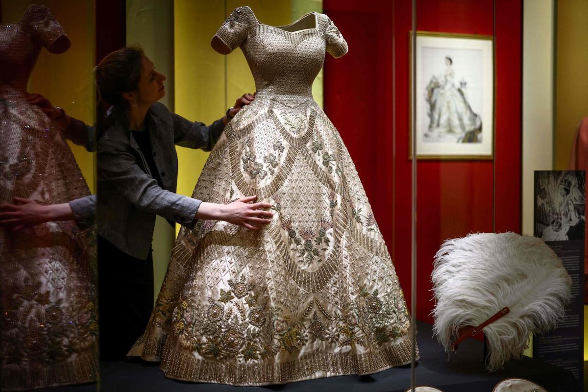 Un miembro del personal del Royal Collection Trust posa con un 'The Coronation Dress' (C) de 1953, durante una vista previa para los medios de la exposición 'Queen Elizabeth II: Her Life in Style' en la King's Gallery en el Palacio de Buckingham en Londres el 9 de abril de 2026. La exposición más grande que jamás haya organizado la moda de la reina Isabel II se llevará a cabo del 10 de abril al 18 de octubre de 2026. (Foto de Henry NICHOLLS / AFP) RESTRINGIDO A USO EDITORIAL - SIN MARKETING - SIN CAMPAÑAS PUBLICITARIAS. RESTRINGIDO A USO EDITORIAL - SIN MARKETING - SIN CAMPAÑAS PUBLICITARIAS