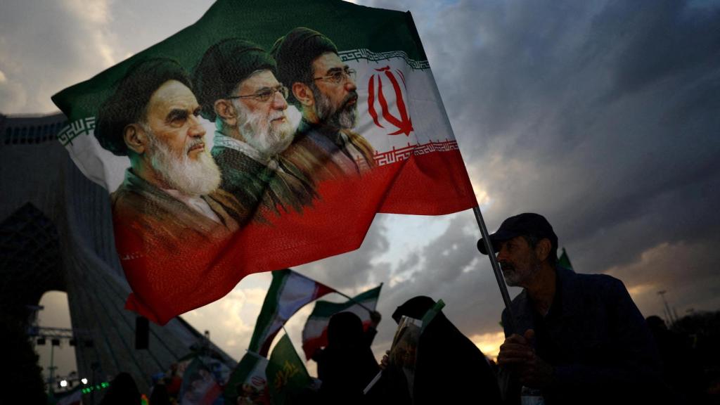 Un hombre sostiene una bandera con una imagen del difunto líder de la Revolución Islámica, el ayatolá Ruhollah Jomeini, el difunto ayatolá Ali Khamenei y el nuevo líder supremo, Mojtaba Khamenei.