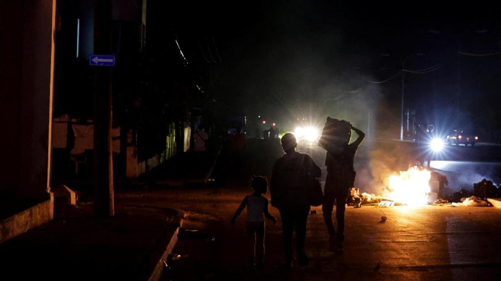 Varias personas caminan junto a basura quemada en medio de una calle durante una protesta contra los frecuentes cortes de energía.