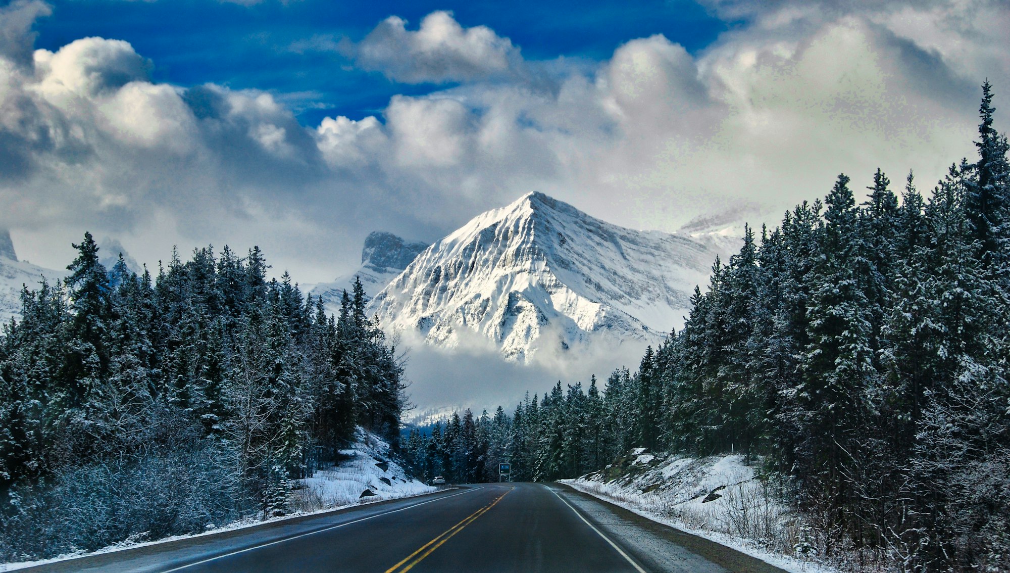 Carretera asfaltada gris cerca de una montaña cubierta de nieve durante el día