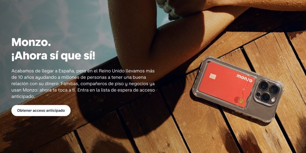 Smartphone iPhone con tarjeta bancaria Monzo roja almacenada en una caja transparente, colocada sobre una superficie de madera junto a la piscina.