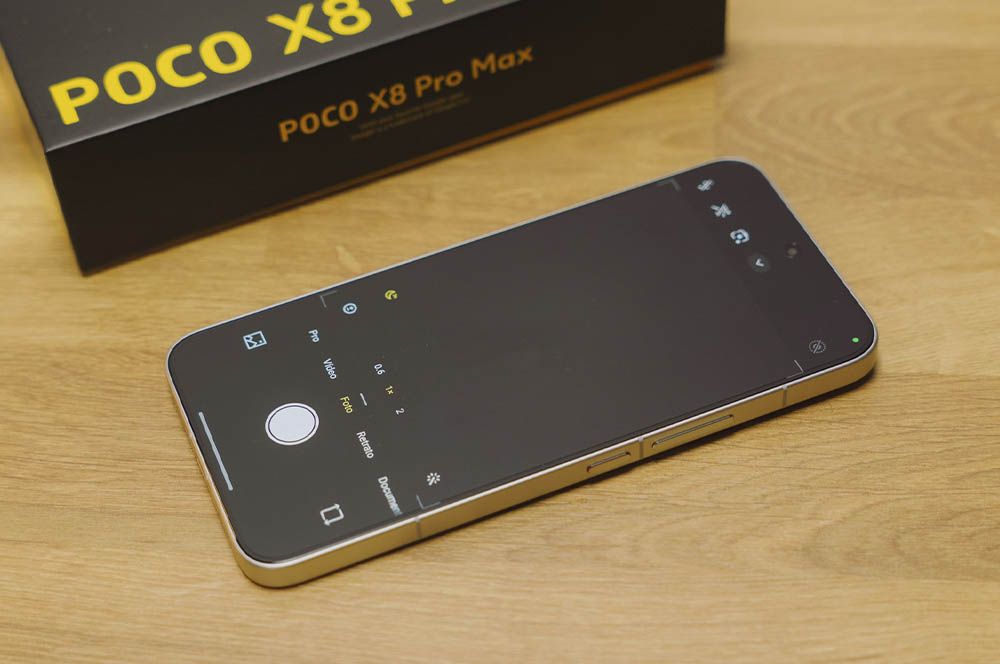 La aplicación de la cámara del teléfono inteligente POCO X8 Pro Max se abre en una mesa de madera junto a la caja original.