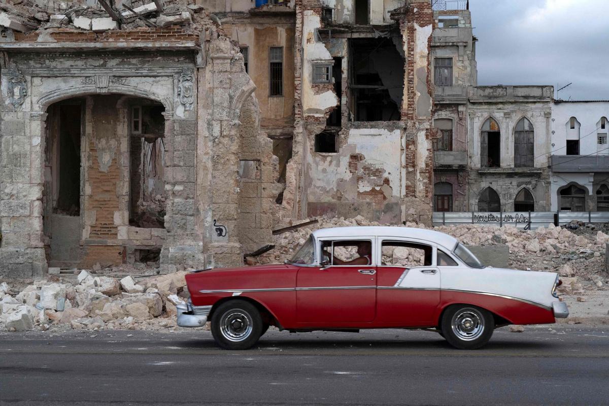 Un vehículo circula junto a una casa con parte de su estructura derrumbada en la calle, en Centro Habana.