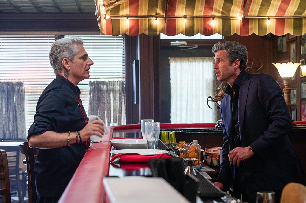 Patrick Dempsey y Michael Imperioli mantienen una tensa conversación en la barra de un restaurante de estilo clásico.