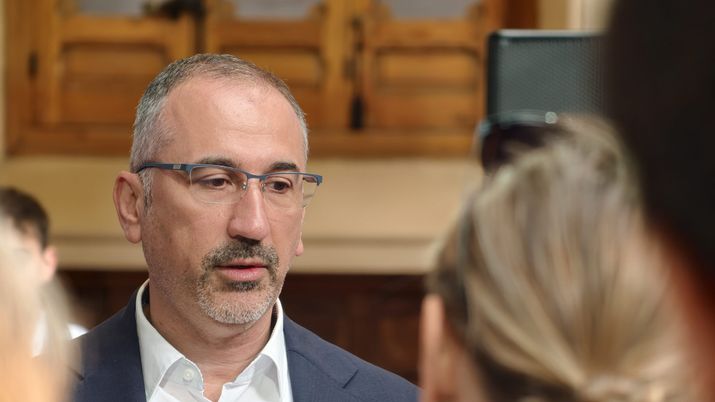 Primer plano de un hombre con gafas y barba gris hablando en un evento o entrevista.