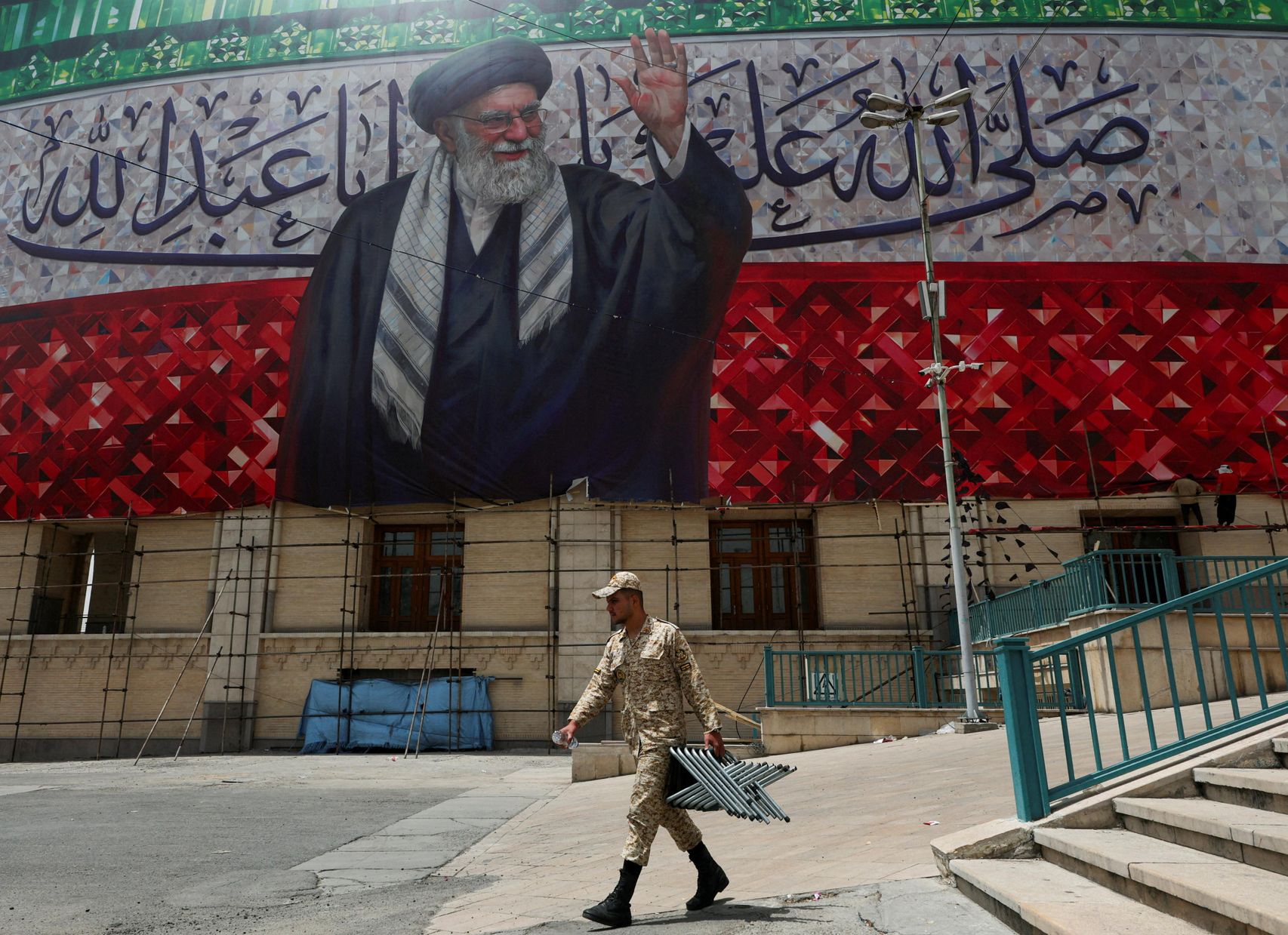 Un miembro de las fuerzas paramilitares Basij lleva piezas metálicas debajo de un gran cartel que representa al difunto líder supremo de Irán, el ayatolá Ali Jamenei.