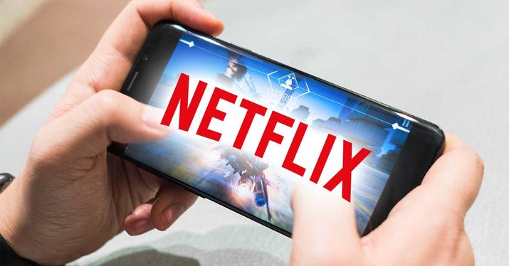 Mano sosteniendo un teléfono móvil horizontal con el logo de Netflix superpuesto en la escena del videojuego.
